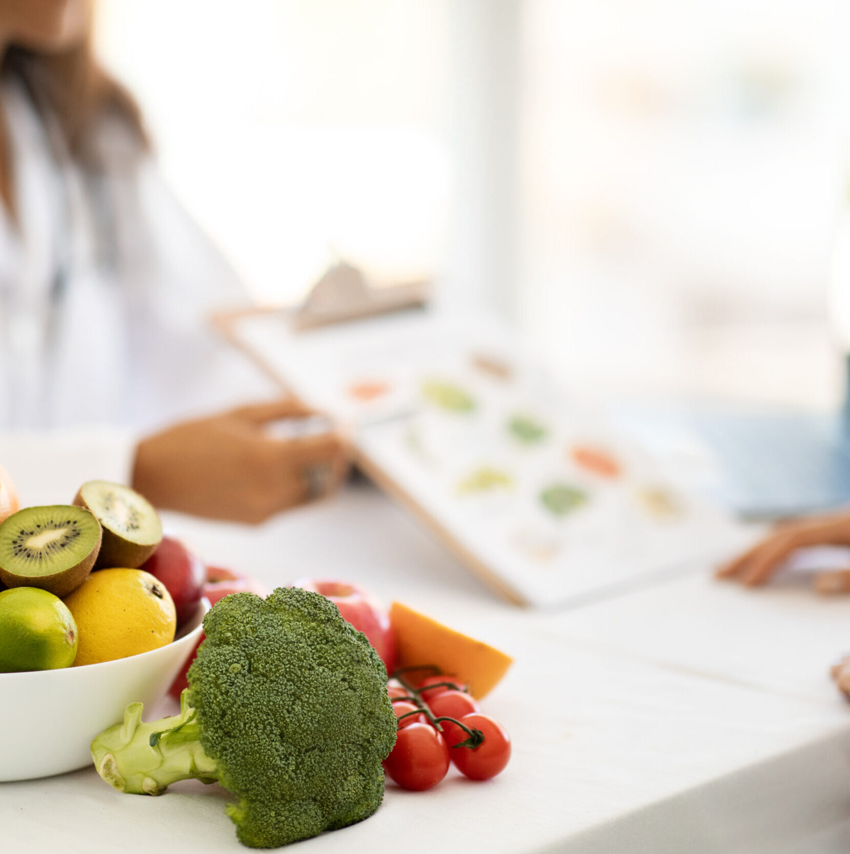 Mature caucasian doctor nutritionist in white coat recommends to young woman diet plan at table with organic vegetables