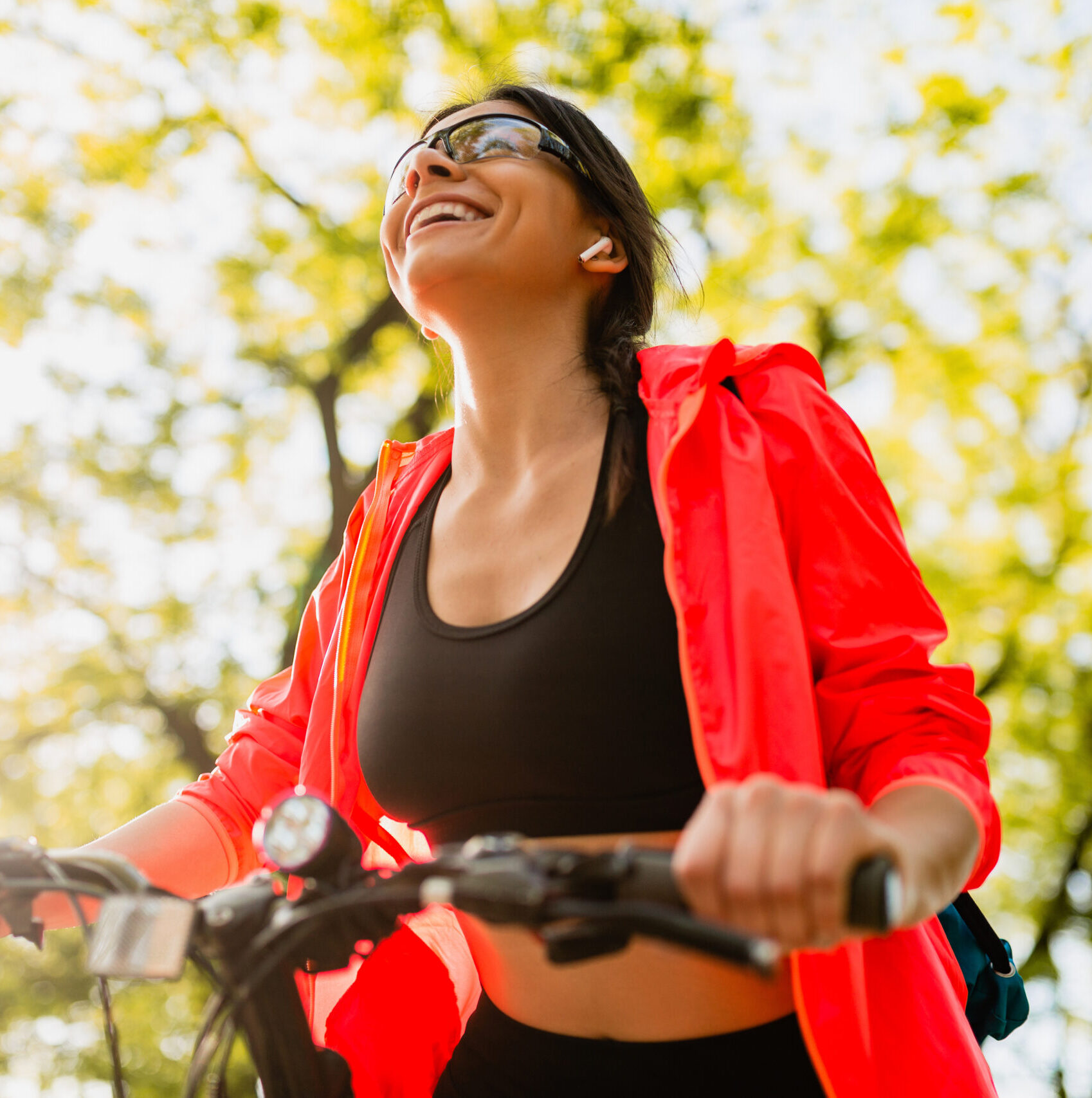 slim fit beautiful woman doing sports in morning in park riding on bicycle on road with yoga mat in colorful fitness outfit, exploring nature, smiling happy healthy lifestyle